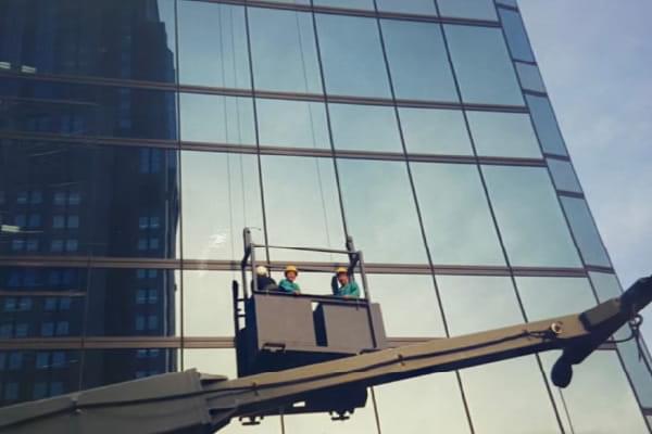 高層ビルの外側でゴンドラに乗り作業をする職人たち
